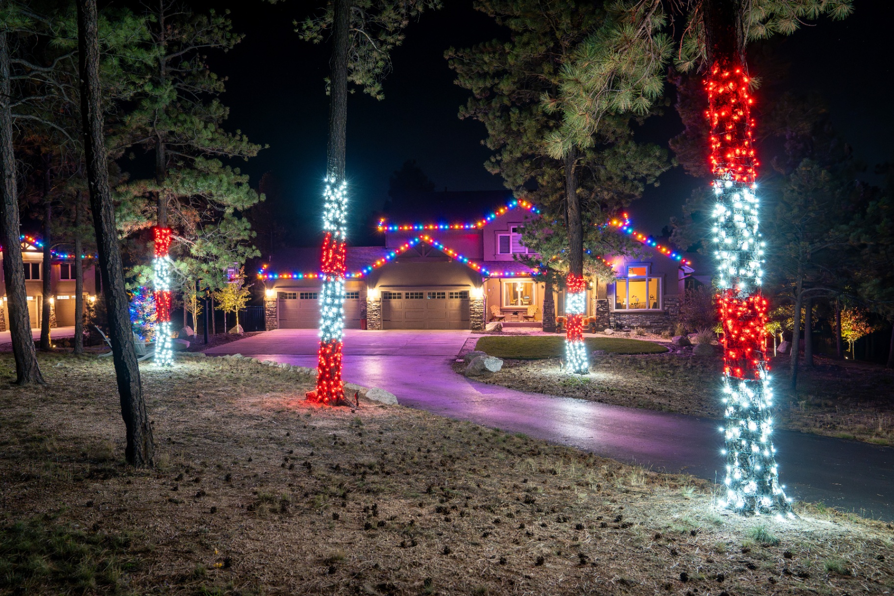 Multicolor roofline lighting with red and white tree-wrapped pines on a mountain home