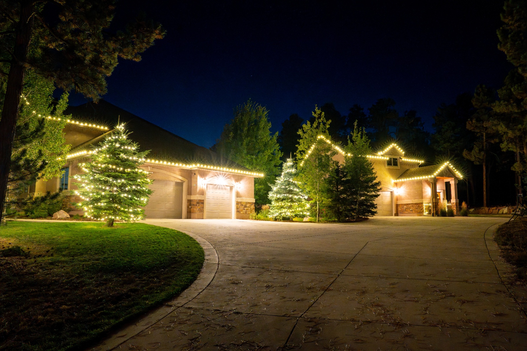 Warm white Christmas lighting on a mountain home with wrapped trees