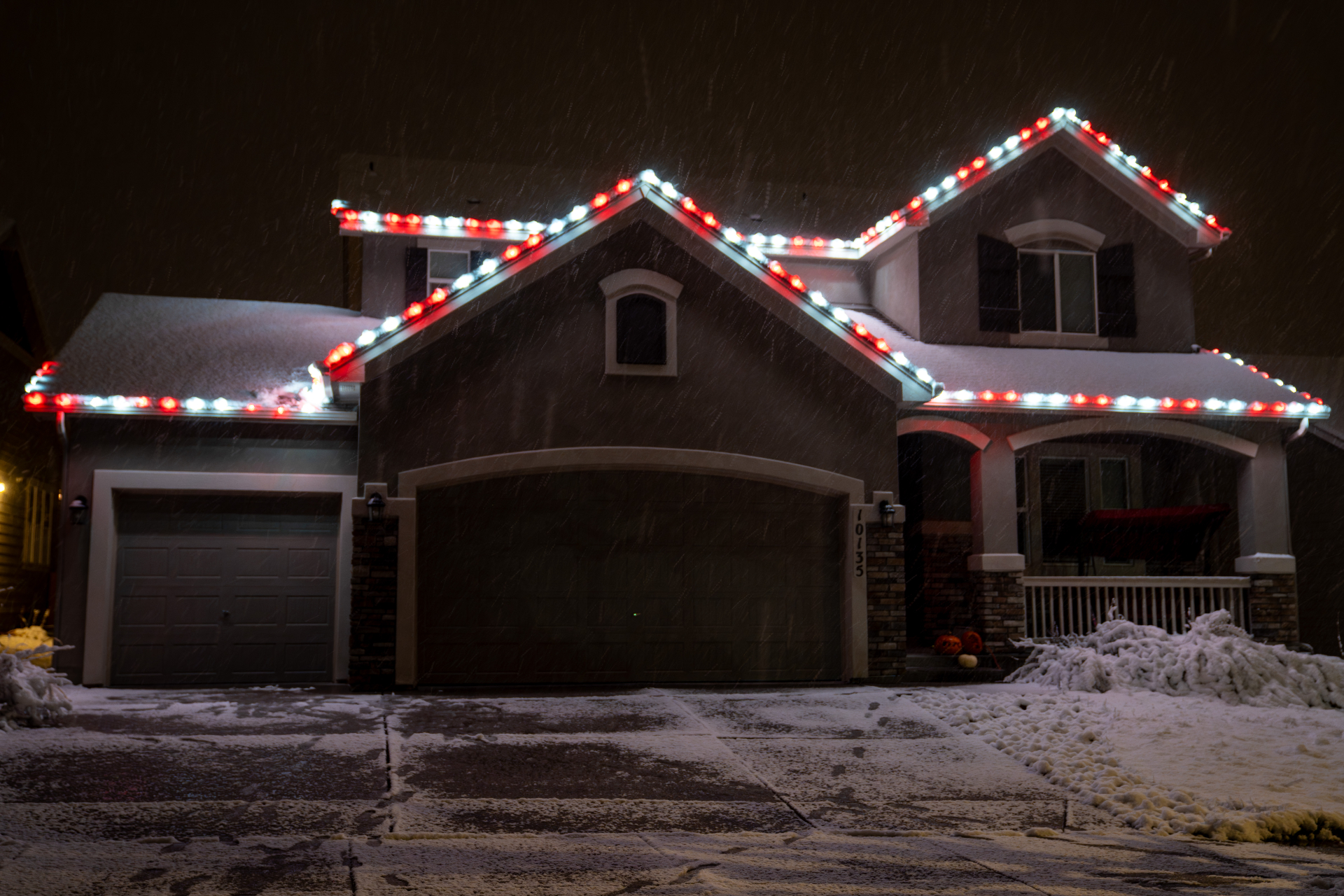 Red and white Christmas lights on a two-story home in falling snow