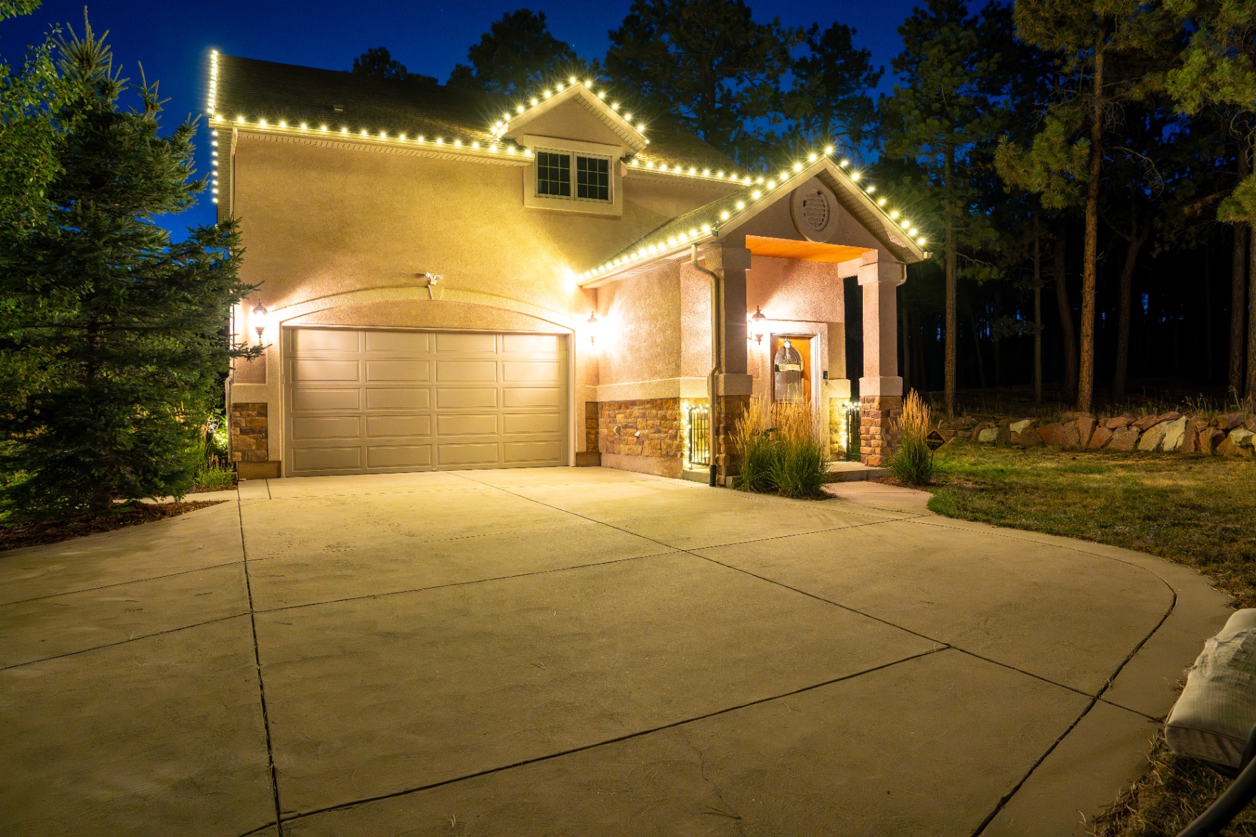 Warm white roofline Christmas lighting on a stucco home at dusk