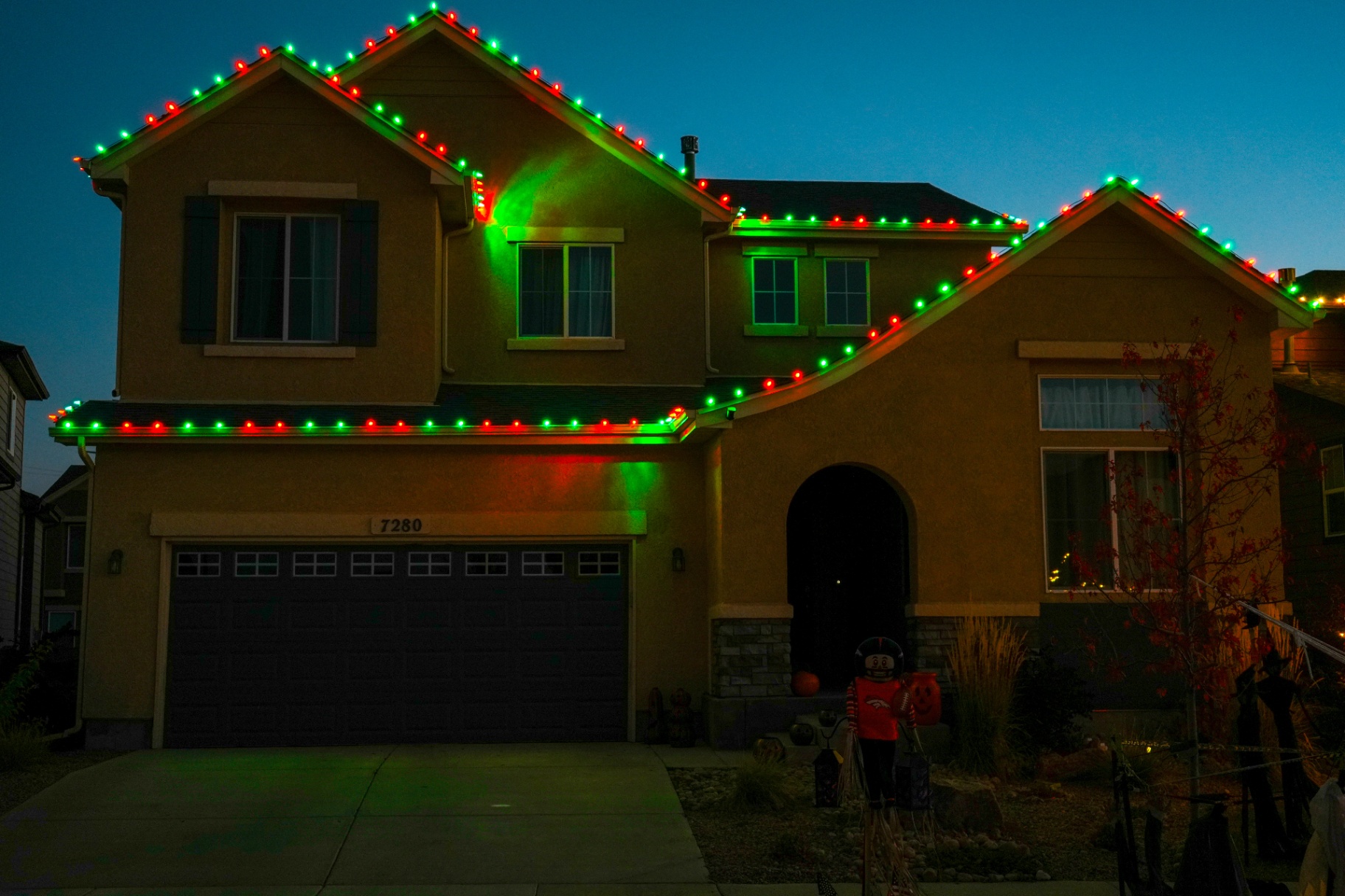 Red and green C9 Christmas lighting on a stucco home at dusk