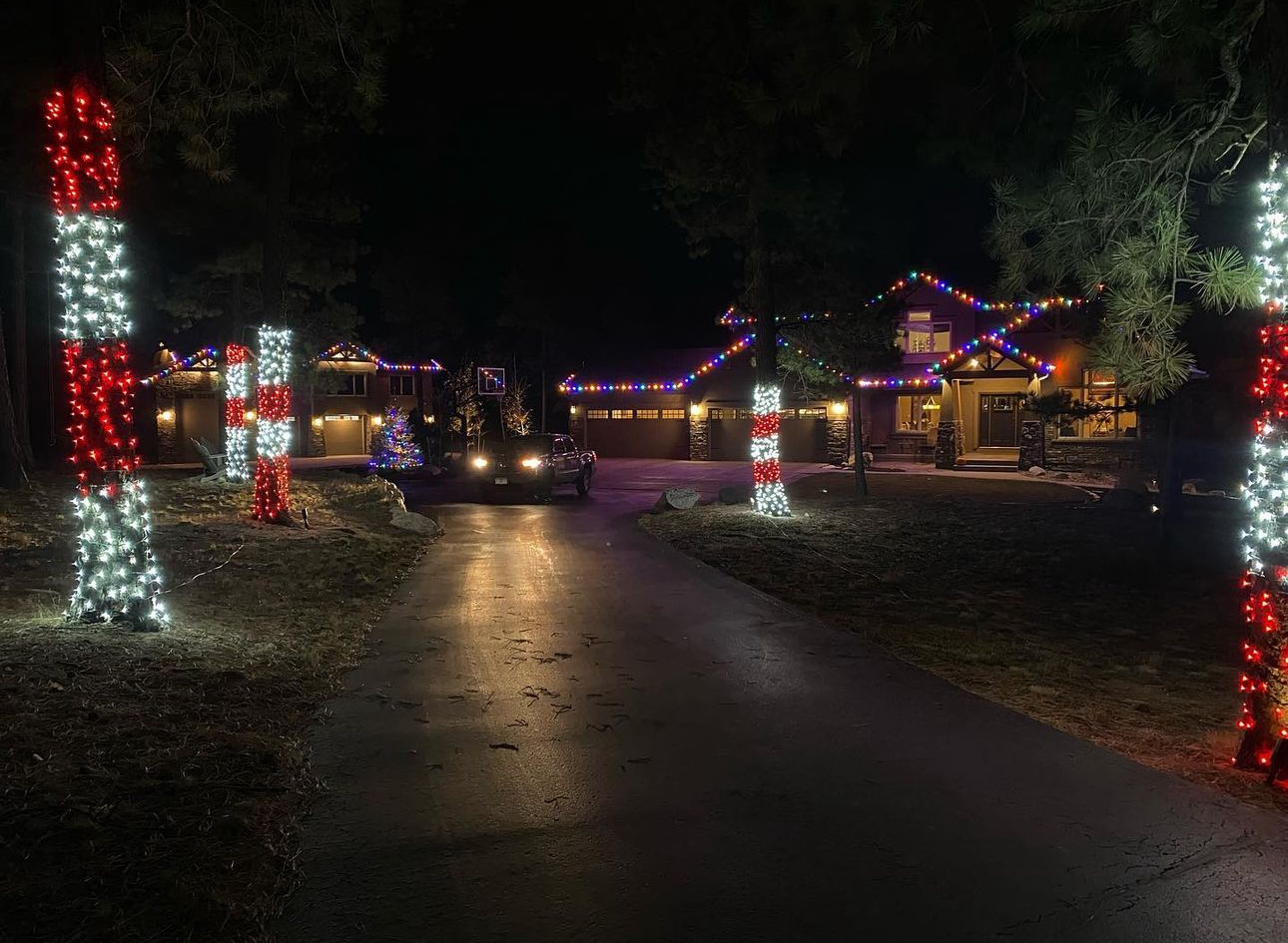 Wide driveway view of multicolor holiday lighting and wrapped trees