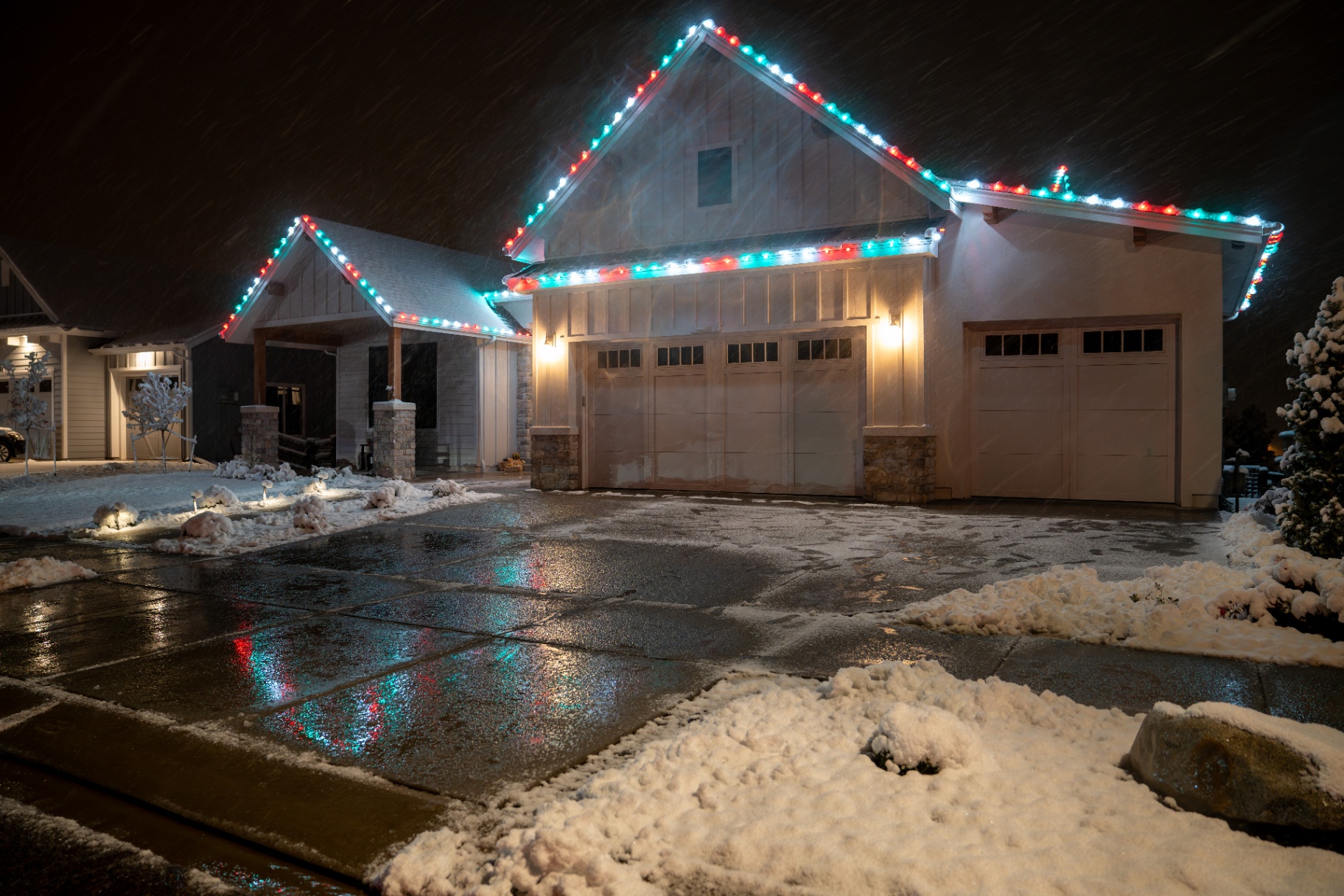Red and green Christmas roofline lighting on a snowy craftsman home