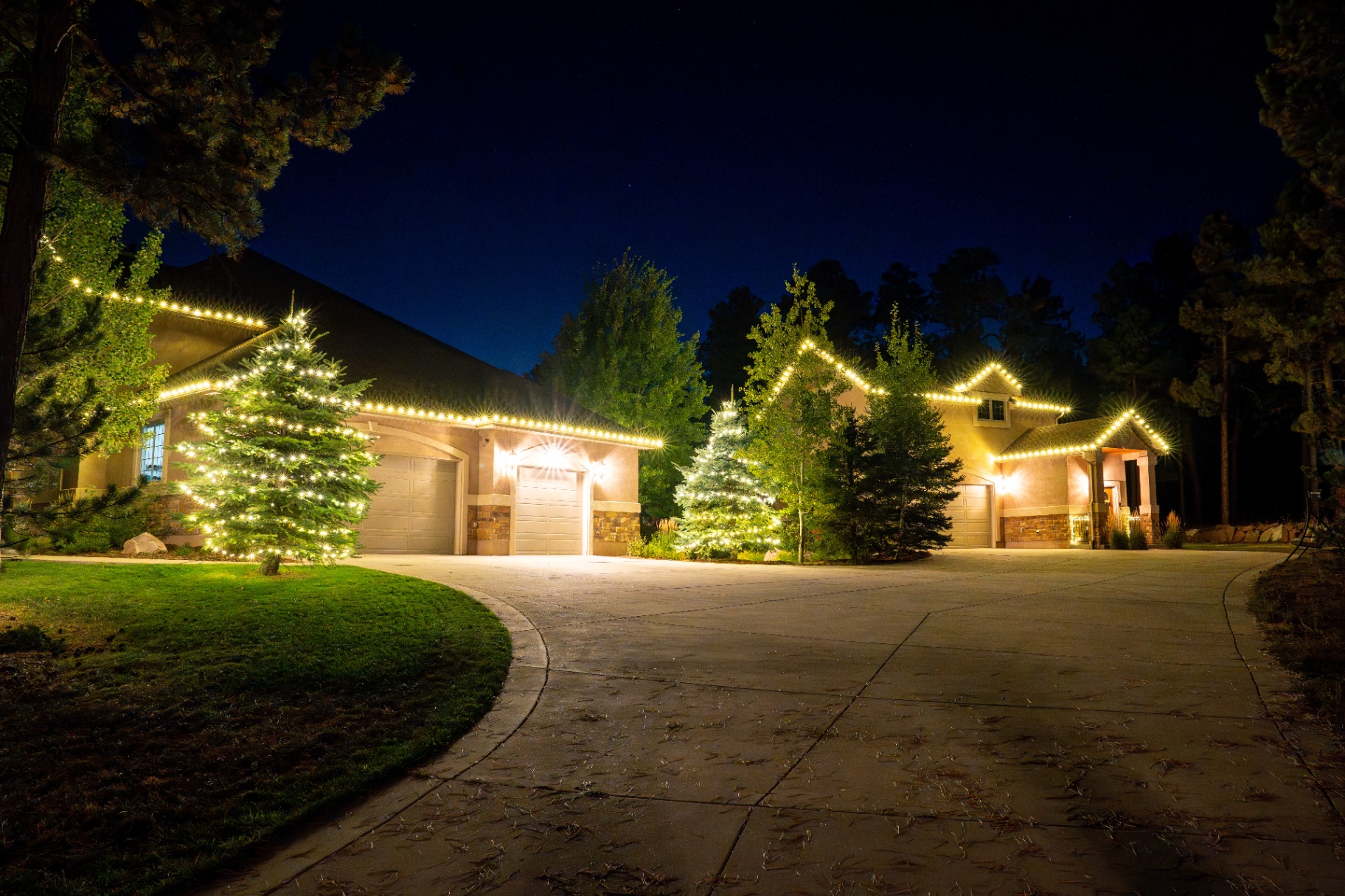 Warm white roofline and tree lighting on a large home at dusk